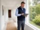 Male home watch professional standing in a bright hallway and using a tablet
